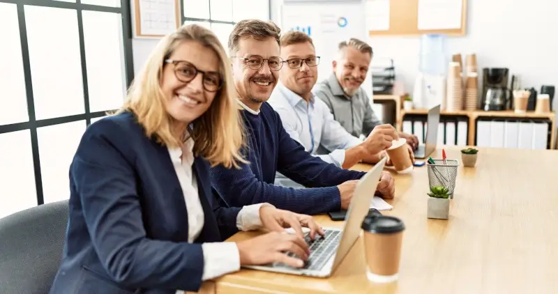 Gruppe von Geschäftsleuten mittleren Alters, die im Büro arbeiten und in die Kamera schauen.