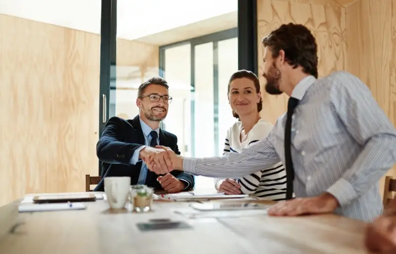 Sealing the deal. Shot of two businesspeople shaking hands in an office while a colleague look on.