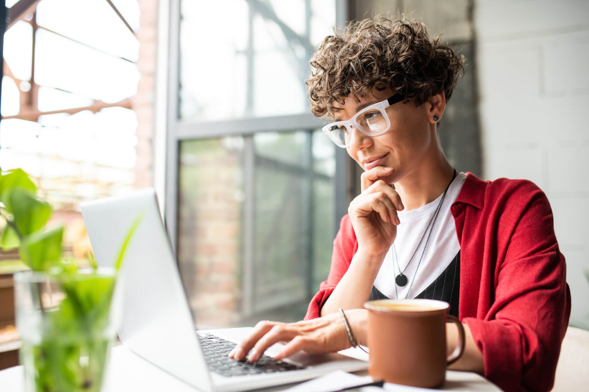 Busy young elegant woman in eyeglasses looking at laptop display